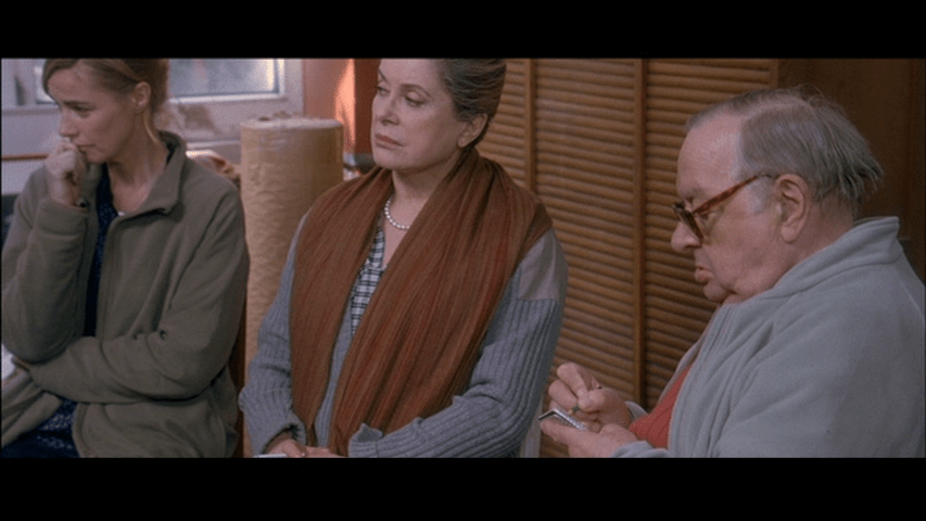 Screengrab from A Christmas Tale showing Abel taking notes on what Claude is saying while Junon and Elizabeth listen