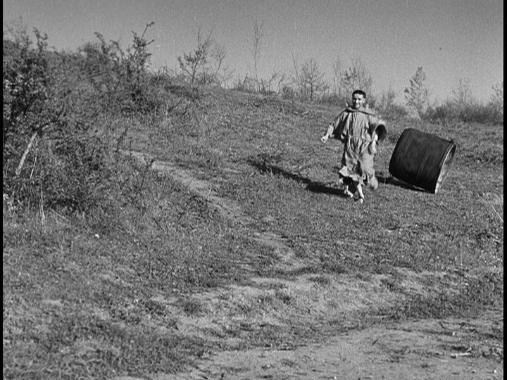 Screengrab from The Flowers of St. Francis showing Brother Ginepro running down a hill trailed by a large kettle