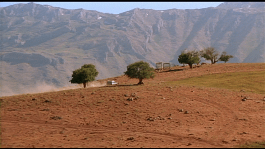 Behzad's car on the increasingly familiar road to the cemetery where he talks on the phone