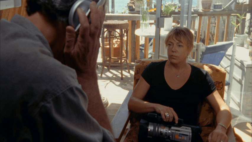 MS of Werner Herzog listening to something with headphones while a woman holding a video camera looks on