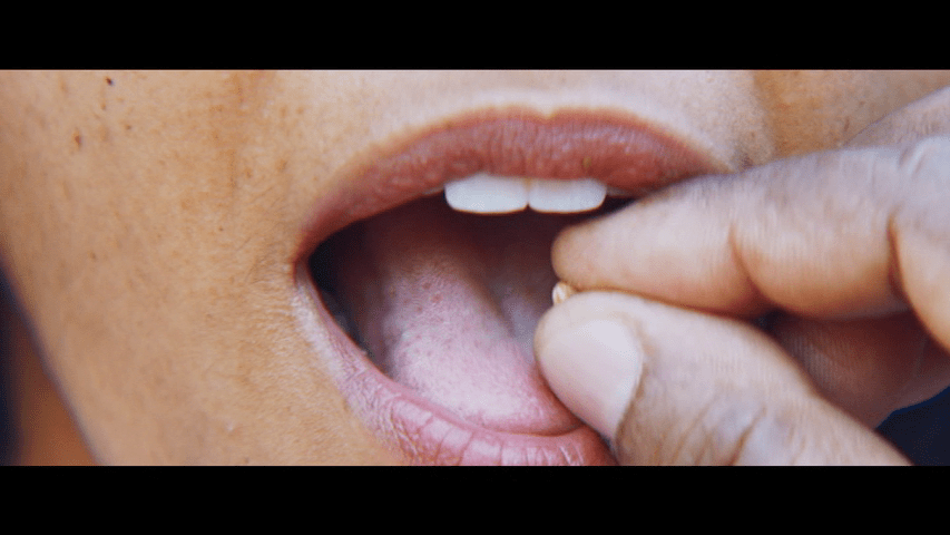 Extreme close up of Damiano administering a psychotropic seed to Teresa