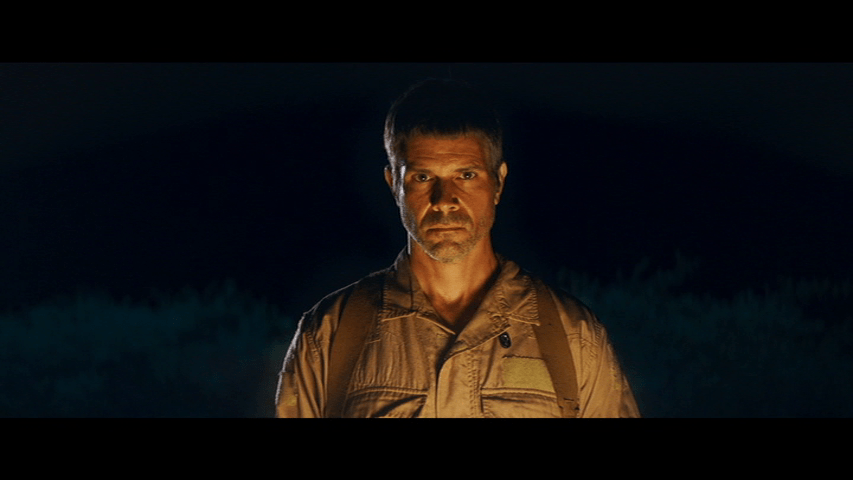 Another medium shot of Joshua, this time lit by the flash of his gun