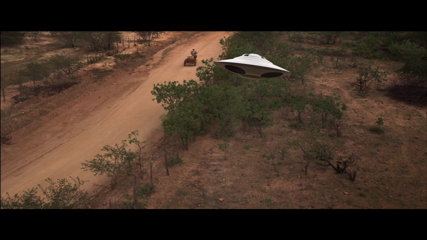A UFO-shaped drone follows a man on a motorcycle