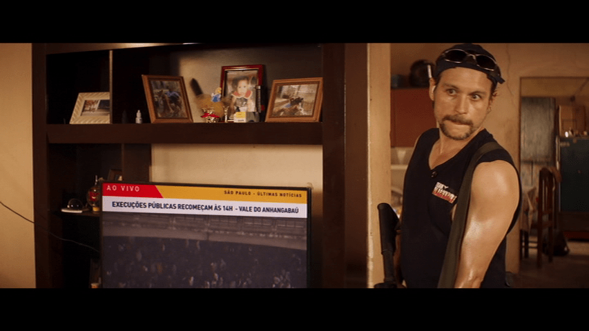 A man with a gun stands in front of a television