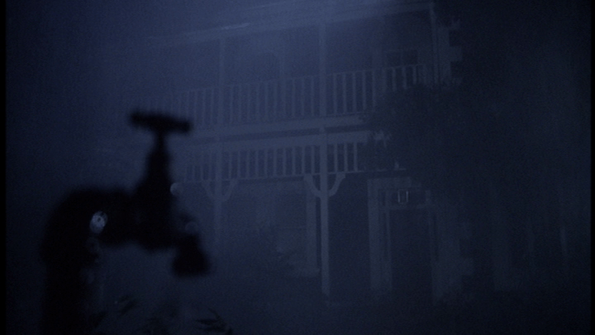 Out-of-focus spigot in the foreground in front of a house on a rainy night