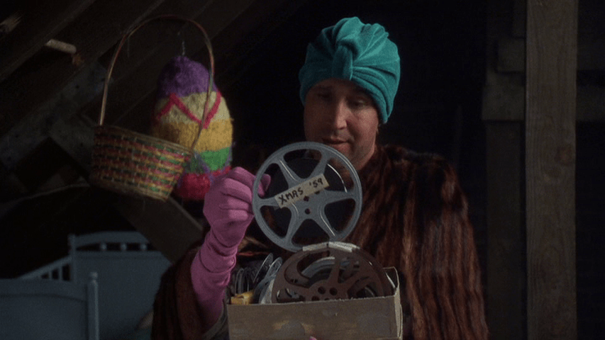 Medium shot of Clark holding a film reel labeled "Xmas '59"