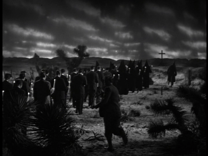 Long shot of a train of hooded marchers with candles