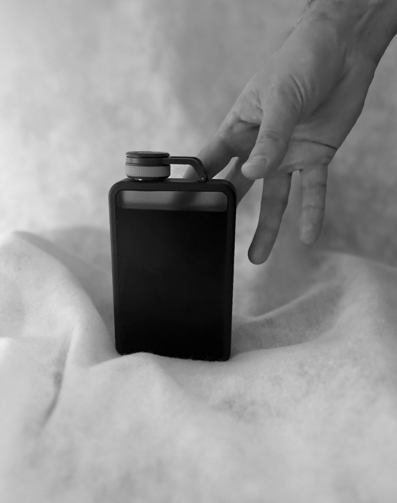Black and white photo of a Pumpernickel cocktail in a flask with a hand reaching for it from above
