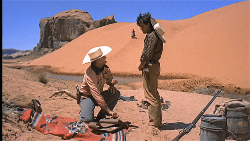 Debbie runs down a distant sand dune toward Ethan and Marty, who are in the foreground