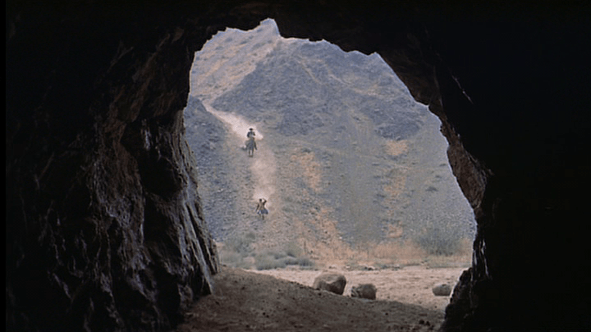 Debbie runs toward a cave in extreme long shot
