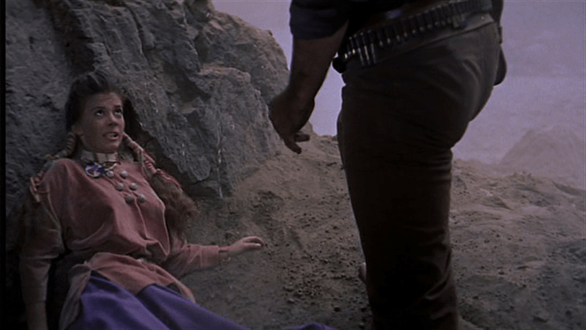 Medium shot of Debbie looking scared as Ethan's legs and torso approach her in the foreground