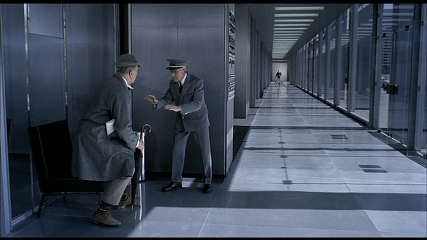 Hulot's first rising, in the foreground of the left side of a bifurcated frame, with a long corridor to the right
