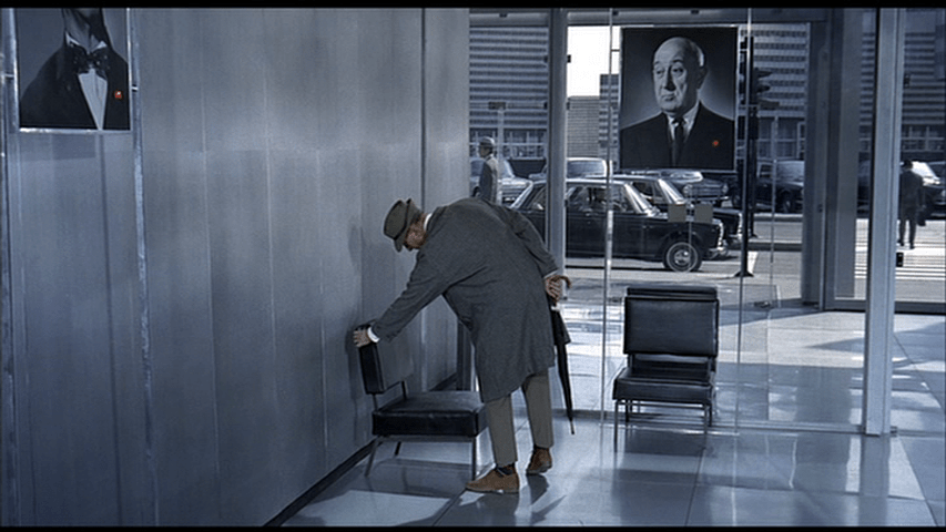 Hulot pushes on the back of a chair while another portrait seems to look askance at him