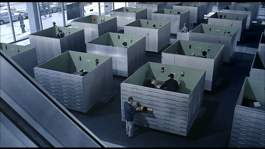 Giffard retrieves a file from the cabinets on the outside of cubicle that Lacs is in...