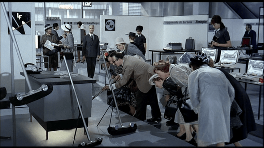 A man demonstrates a broom with headlights to a group of admiring American tourists