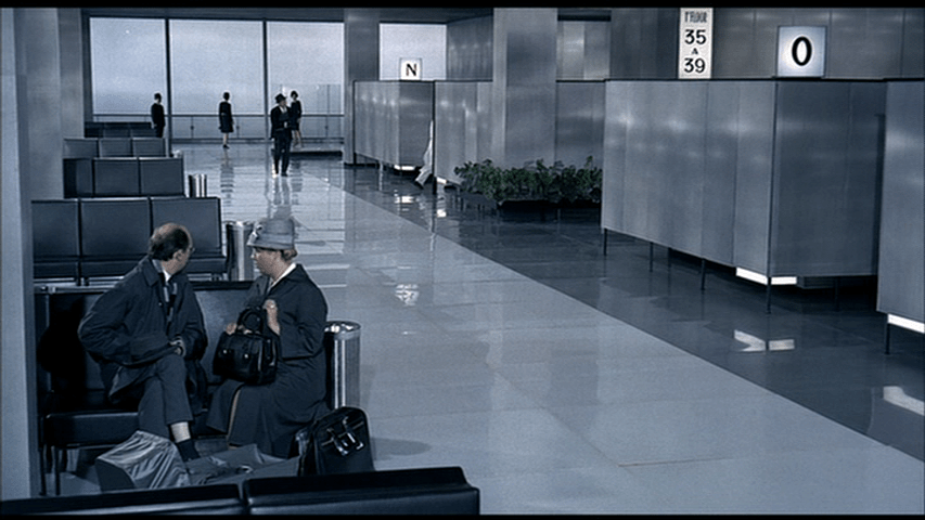 The man and the woman in the foreground look at a man in a suit in the background...