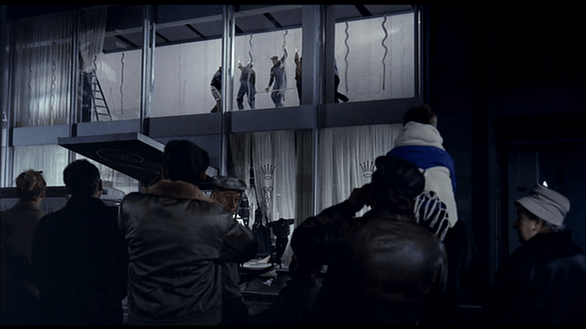 Extreme long shot of construction workers moving a window, who look like they are performing some kind of dance