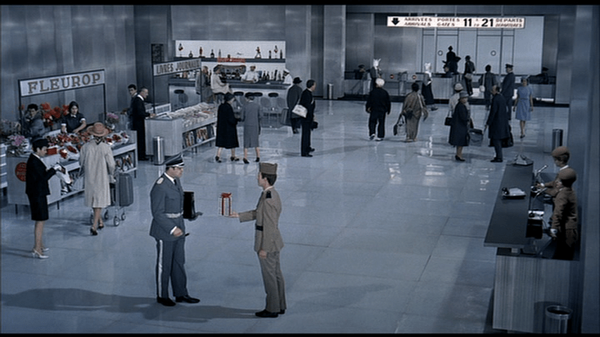 An officer presents his superior with a gift wrapped in a red bow in the foreground of a crowded composition