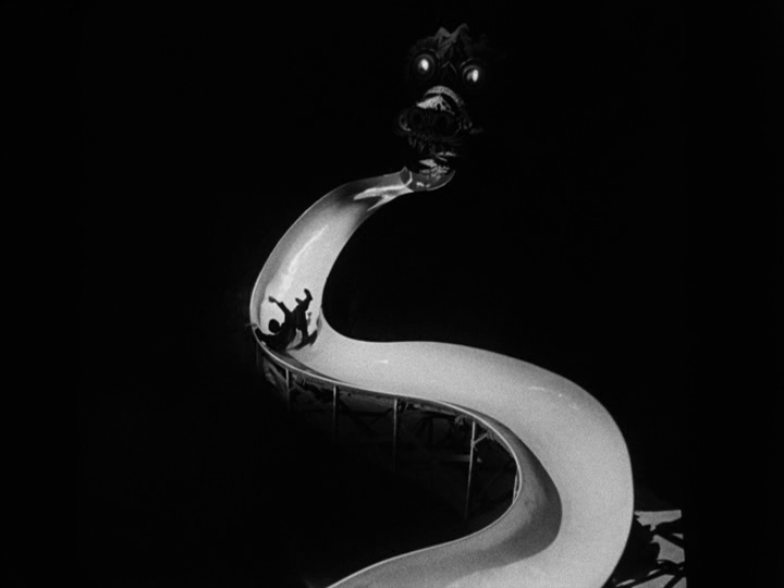 Long shot of Michael tumbling down a long, twisting slide toward a dragon face