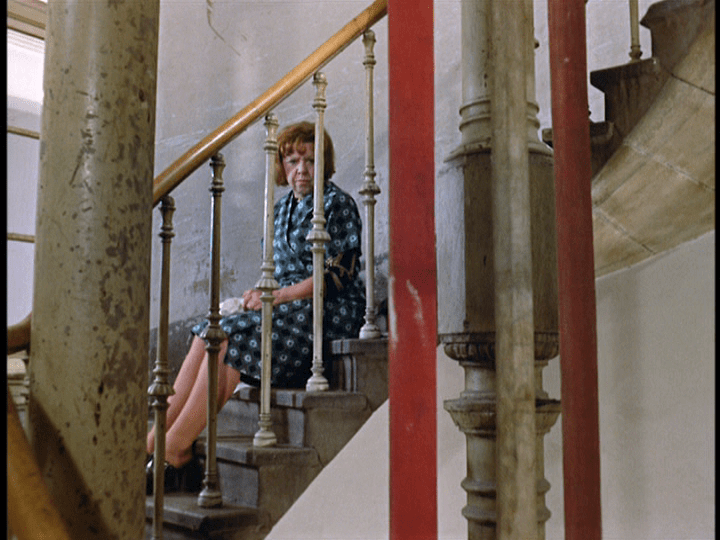 Long shot of Emmi with her lunch on a stairwell behind a railing