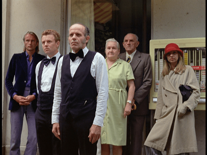 A crowd of waiters and customers stare at Ali and Emmi