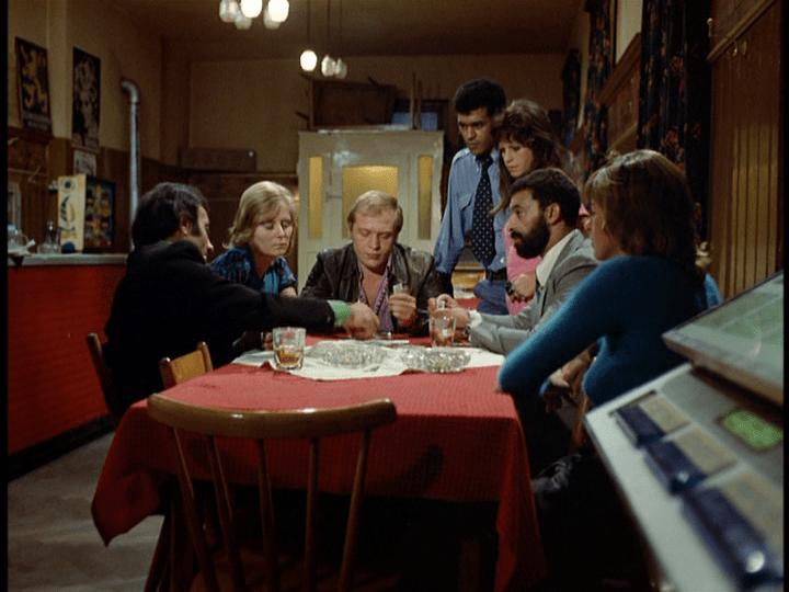 Long shot of Ali seated at a table in the Asphalt Bar playing cards