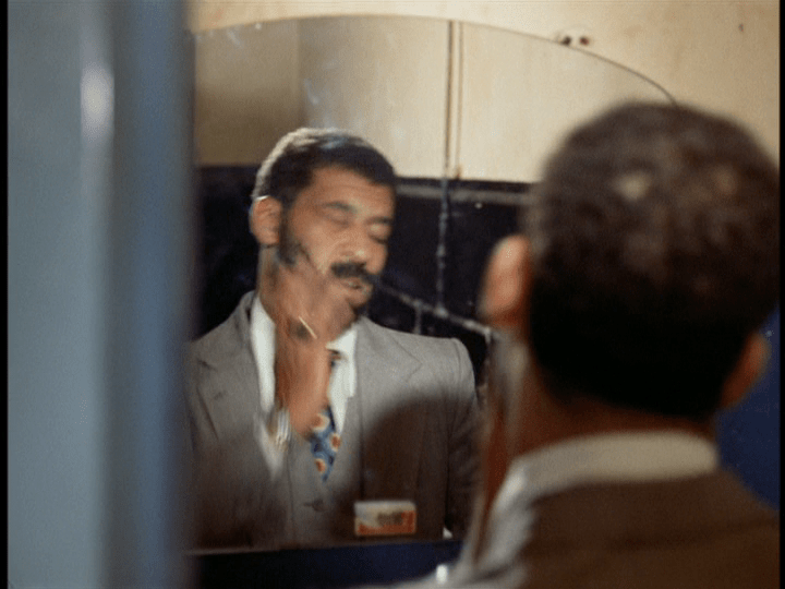 Medium shot of Ali slapping himself in the face as he looks in a mirror