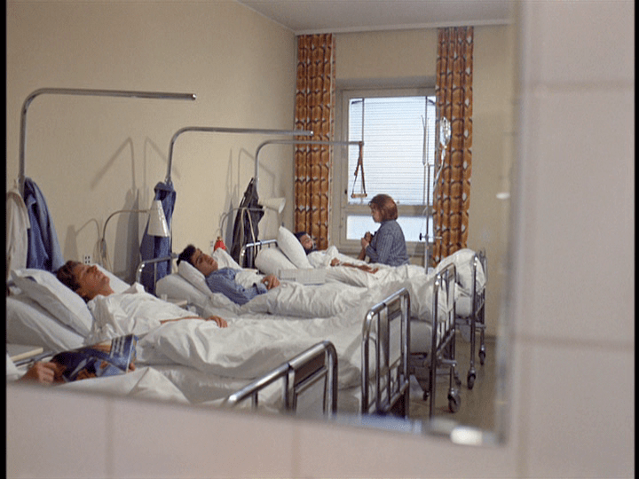 Long shot of Emmi holding Ali's hand reflected in a mirror