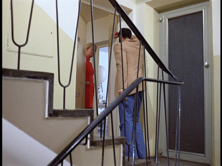 Ali and his mistress Barbara are shown in long shot through a railing as she opens the door of her apartment to him