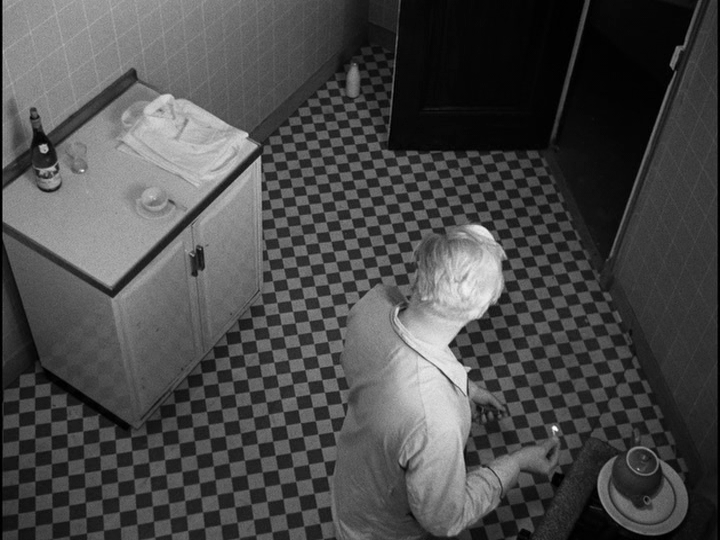 Bob pauses while lighting the stove on the other side of the room to look back at the bottle