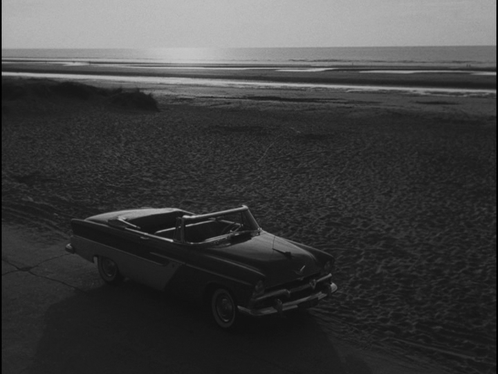Long shot of Bob's car in the bottom 1/3 of the frame and the coast in the top 1/3 of the frame, with empty sand in between