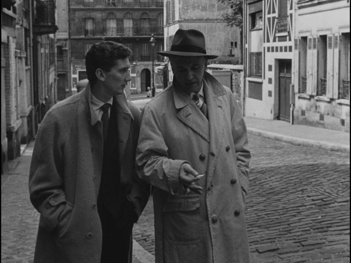 Medium shot of Bob regaling Paolo, who is dressed similarly, about a bad bead