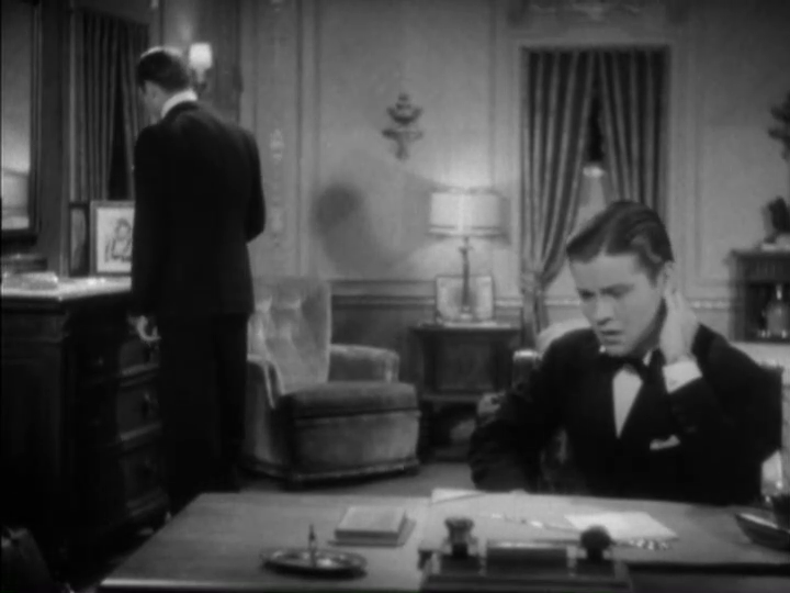 Curtis looks stressed in the foreground while Dugan spies a framed set of photos in the background