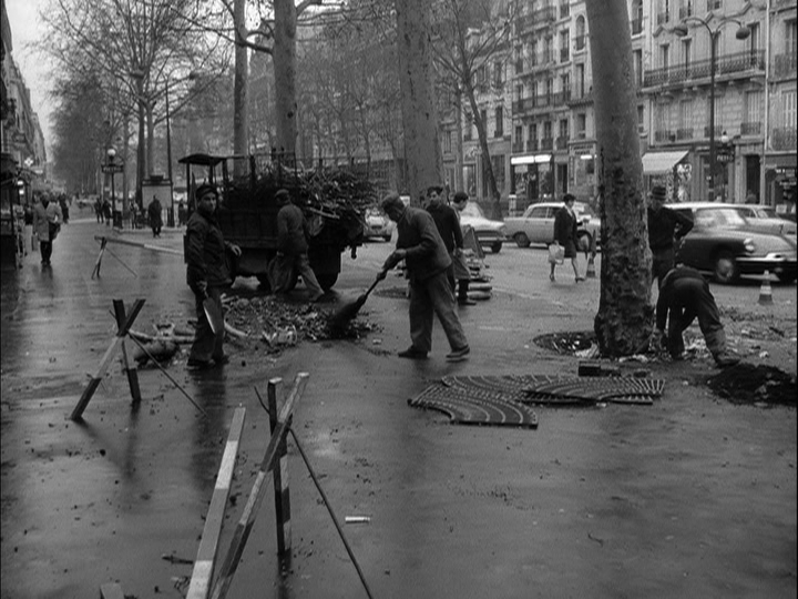 Daytime shot of public works employees cleaning a city street wet from rain