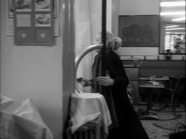 In a continuation of the previous shot, the woman aims her gun through the doorway of the café