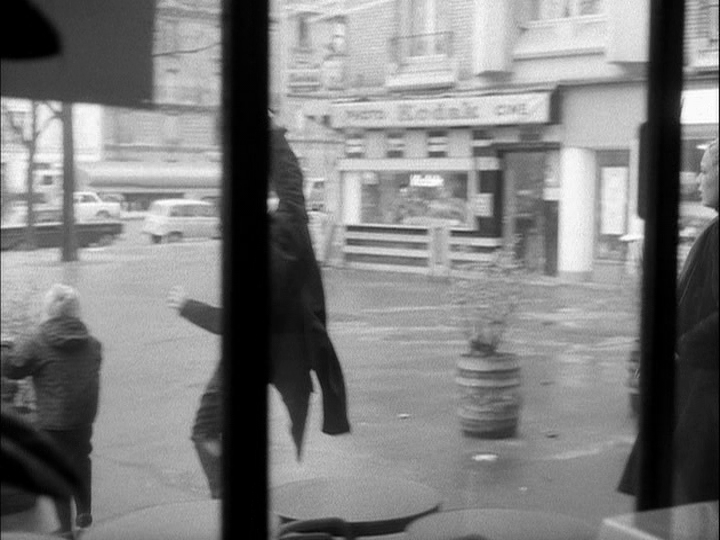 Exterior long shot through the window of the café of a man being shot