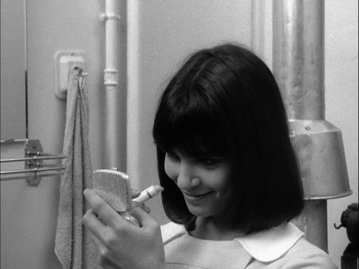 Close-up of Madeleine looking in a compact and putting lipstick on