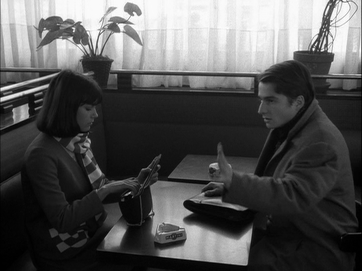 Medium shot of Paul raising his hand in frustration on the right side of the frame because the table he and Madeline, who is on the left side of the frame, are now sitting at still doesn't meet his standards