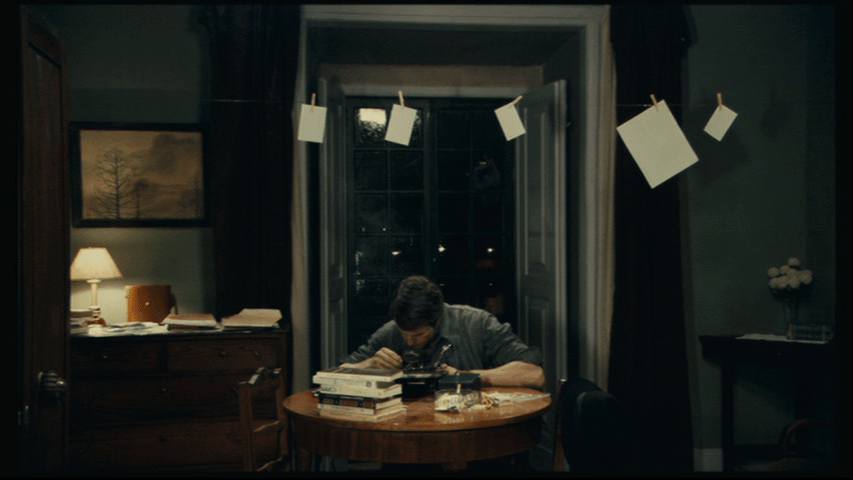 Isaac, framed by a doorway, fiddles with a radio in front of a pile of books
