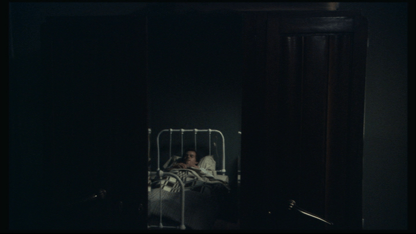 Isaac in bed in the middle of the bottom third of the frame with darkness all around him