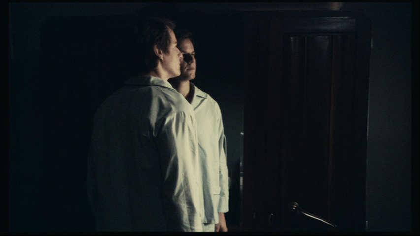 Medium shot of Isaac and his reflection in the middle of the frame