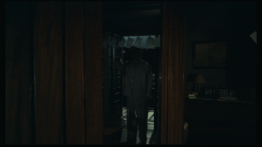 Medium shot of Isaac, still reflected in a mirror, looking at the photos hanging on a line in front of his balcony