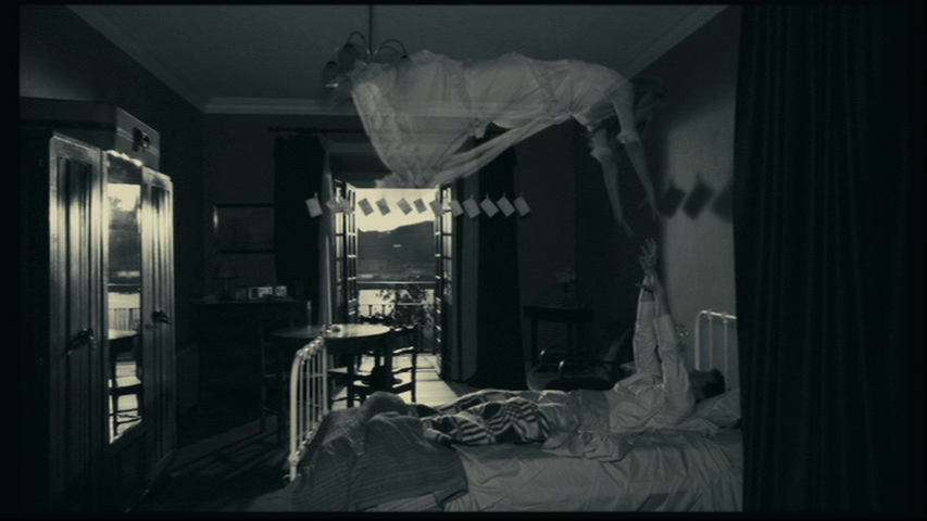 Long shot of Isaac in bead reaching for Angelica's spirit, which hovers over him out of reach