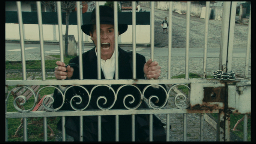 Medium shot of Isaac holding on to the gate to the cemetery where Angelica is buried and shouting her name