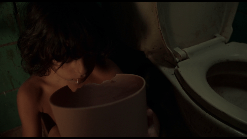 Close up of Brecken sitting on the floor next to a toilet eating the plastic wastebasket as foamy white drool trickles out of the corner of his mouth