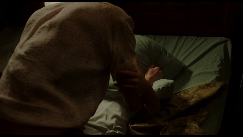 Medium shot of Djuna's back as she holds a pillow over Brecken's face