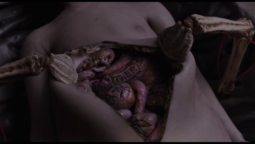 Close-up of the Sark autopsy module opening up Brecken's body to reveal a set of tattooed organs, indicating that whatever was there before has been replaced
