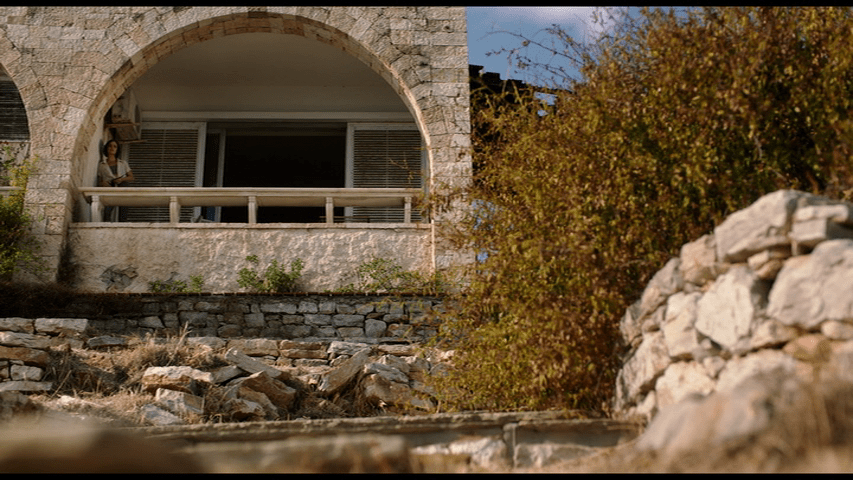 Extreme long shot of Djuna standing on a balcony beneath an archway