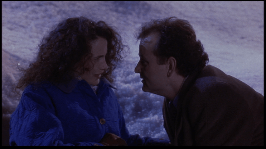 Bill Murray's decidedly *not* debonair Phil Connors unsuccessfully attempts to steal a kiss from Andie MacDowell's Rita Hanson as they both lie in the snow