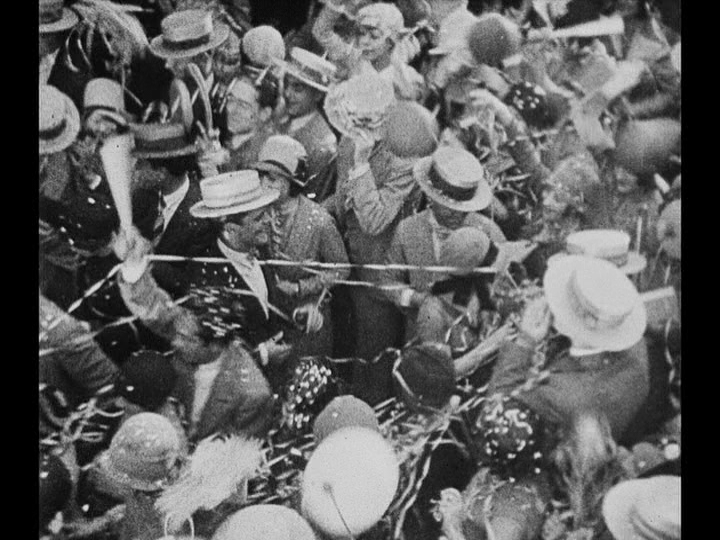 Overhead long shot of Jim following Mary through a crowd
